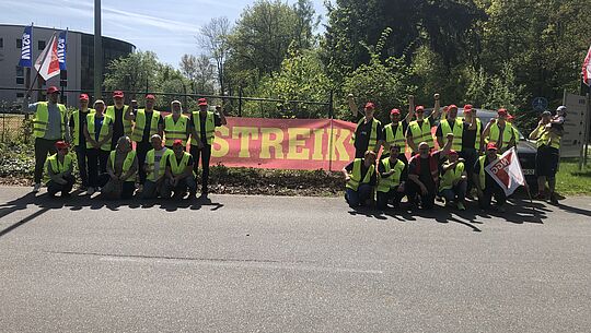 Eine Gruppe Streikender mit einem großen Transparent in der Mitte auf dem "Streik" steht.